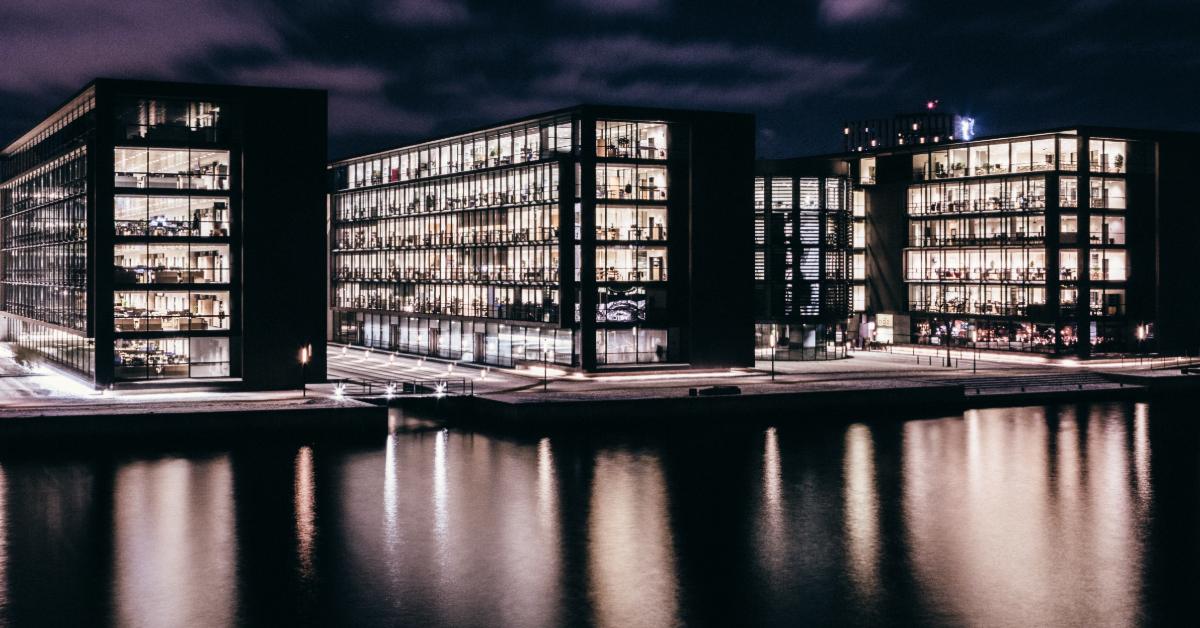 Business buildings at night with lights reflecting off water.