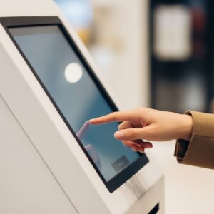 Alt Tag: Hand interacting with a digital kiosk touchscreen for a quick transaction.